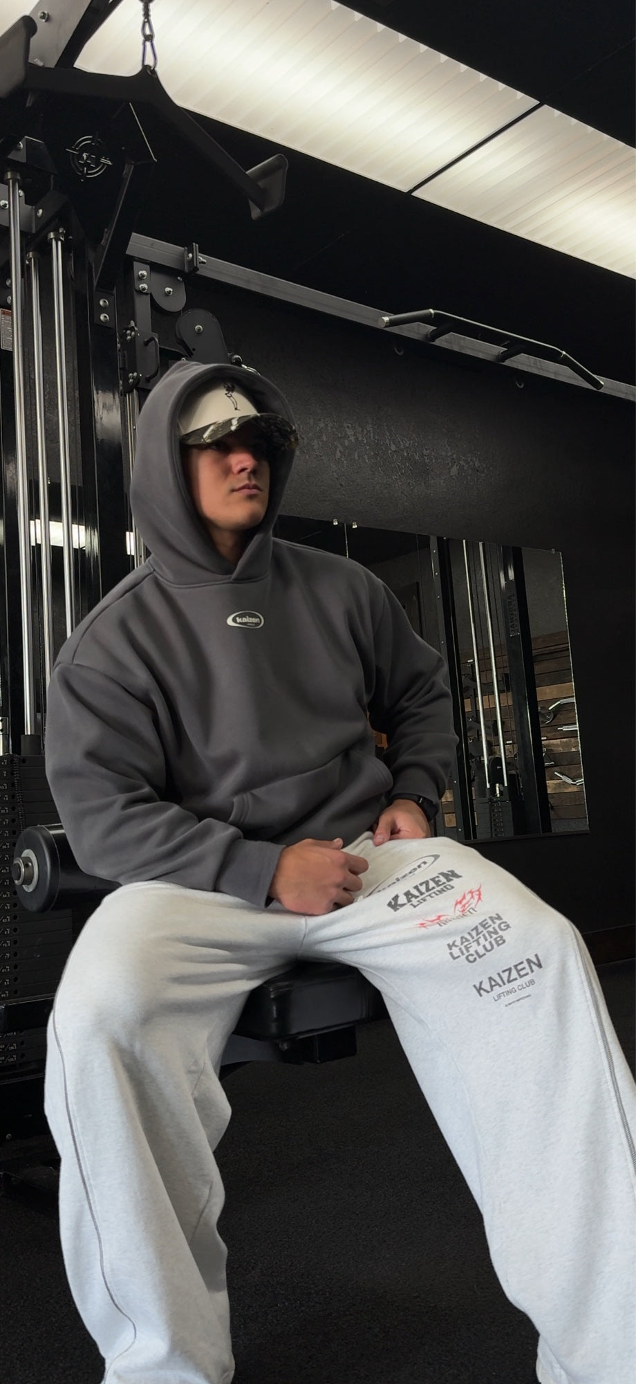 Athlete wearing a charcoal Kaizen hoodie and light gray graphic sweatpants in a gym.